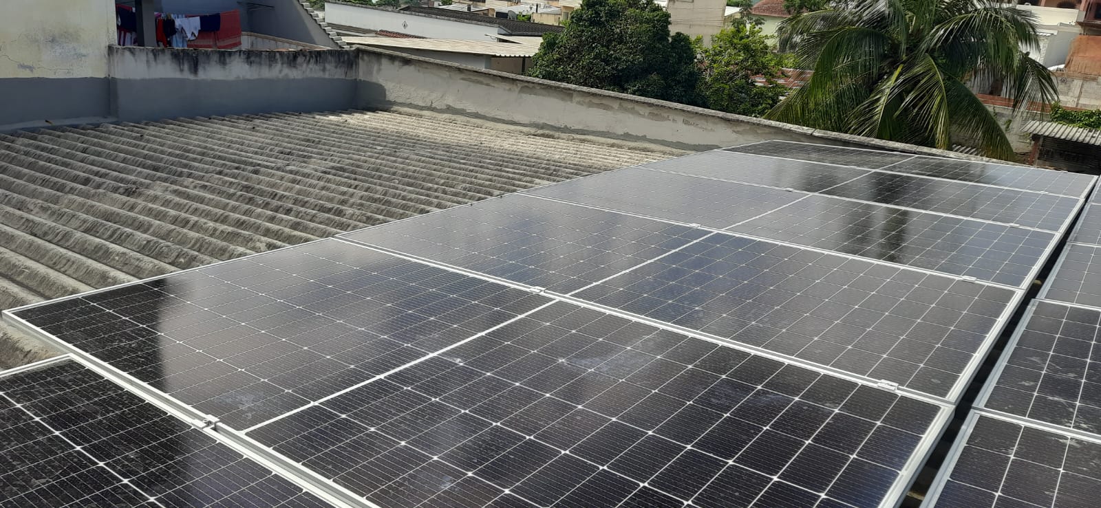 Painéis solares instalados em telhado com vista para palmeiras e vizinhança